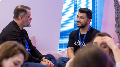 imagem de dois homens de pele branca conversando. Um deles de cabelos e barba grisalhos e outro de cabelo e barba pretos.